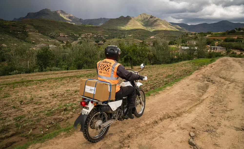 An overlanding traveler standing by their vehicle overlooking a vast mountain range.