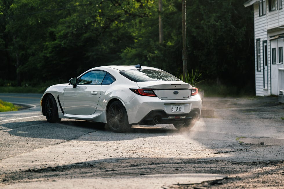 A white Subaru BRZ tS accelerating rapidly along a straight rural road with motion blur.