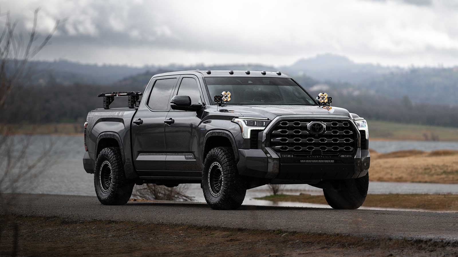 A Toyota Tundra equipped with a truck bed camper and off-road modifications parked in a scenic valley.