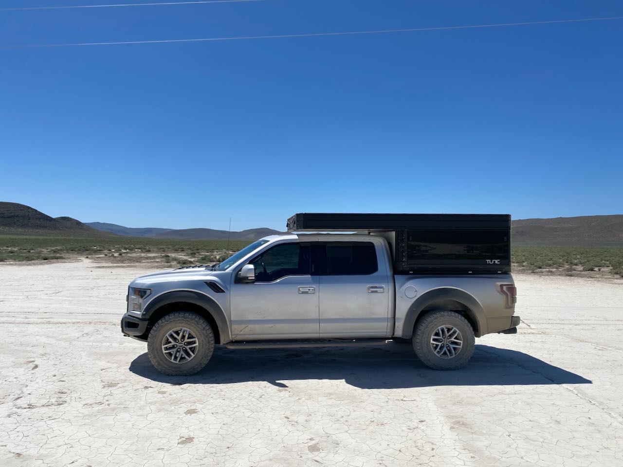 A Ford Raptor truck with a Tune camper driving through a dusty off-road desert trail.