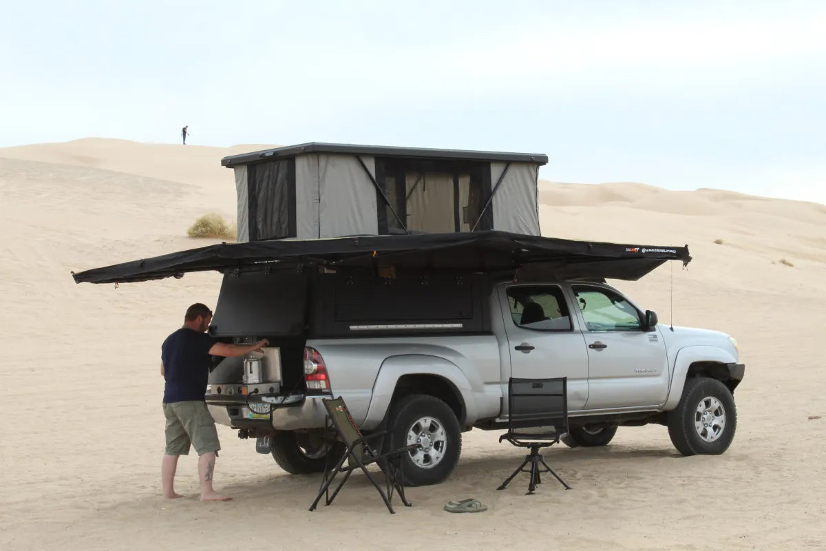Off-road truck camper with a wedge-style pop-top topper navigating desert sand dunes.