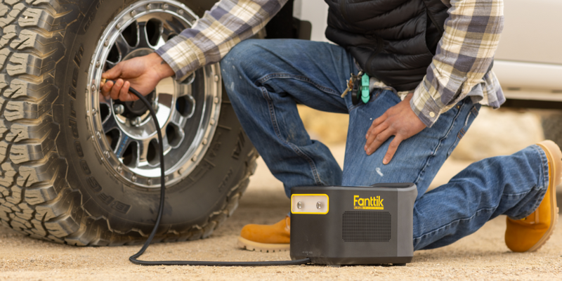 A person using a compact Fanttik portable tire inflator on a large off-road tire.