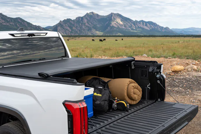 Close-up of a black tonneau cover protecting cargo on a truck driving through dirt terrain.