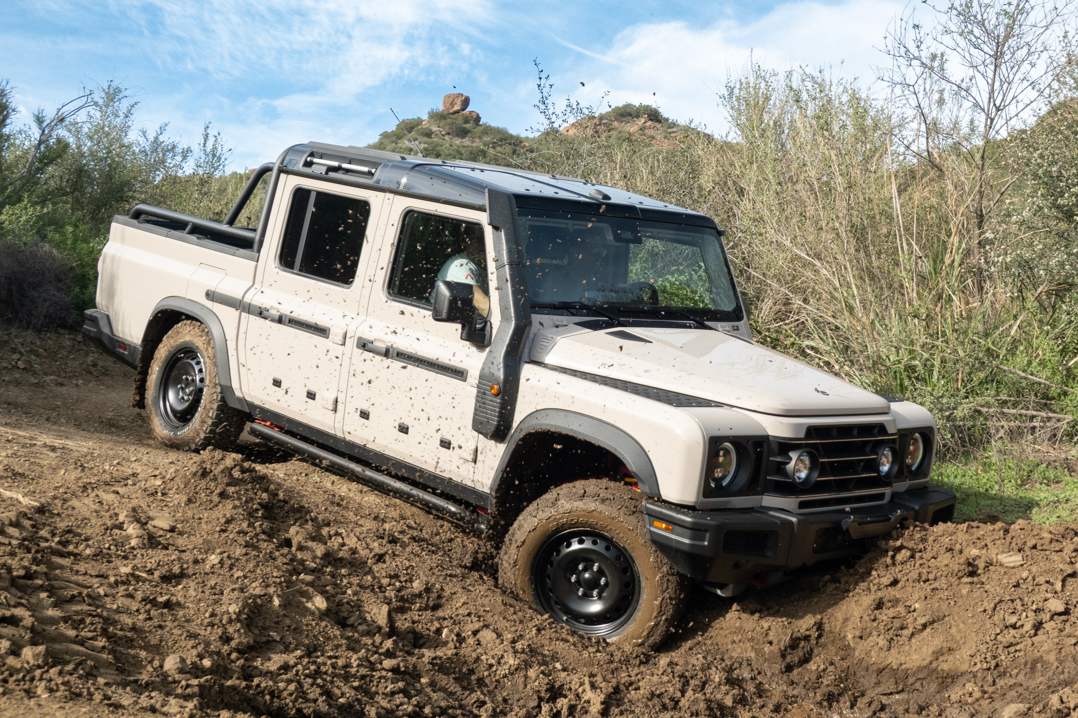 An Ineos Grenadier Quartermaster pickup truck driving on a dirt trail.