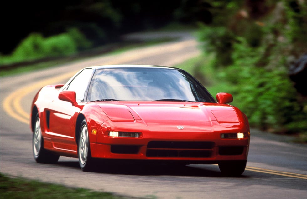 A red 1993 Acura NSX driving on a winding backroad surrounded by trees.