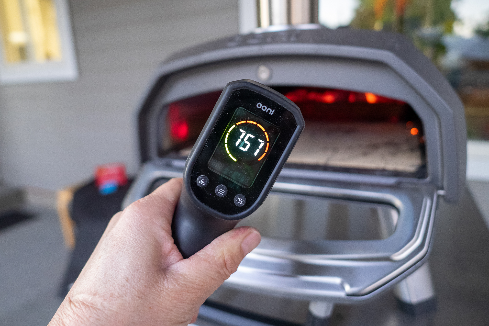 An Ooni Karu pizza oven positioned on a wooden table at a campsite with a forest background.