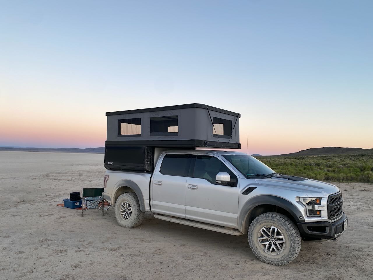 Rear view of a pickup truck with the Tune camper open and the tailgate down in a desert campsite.