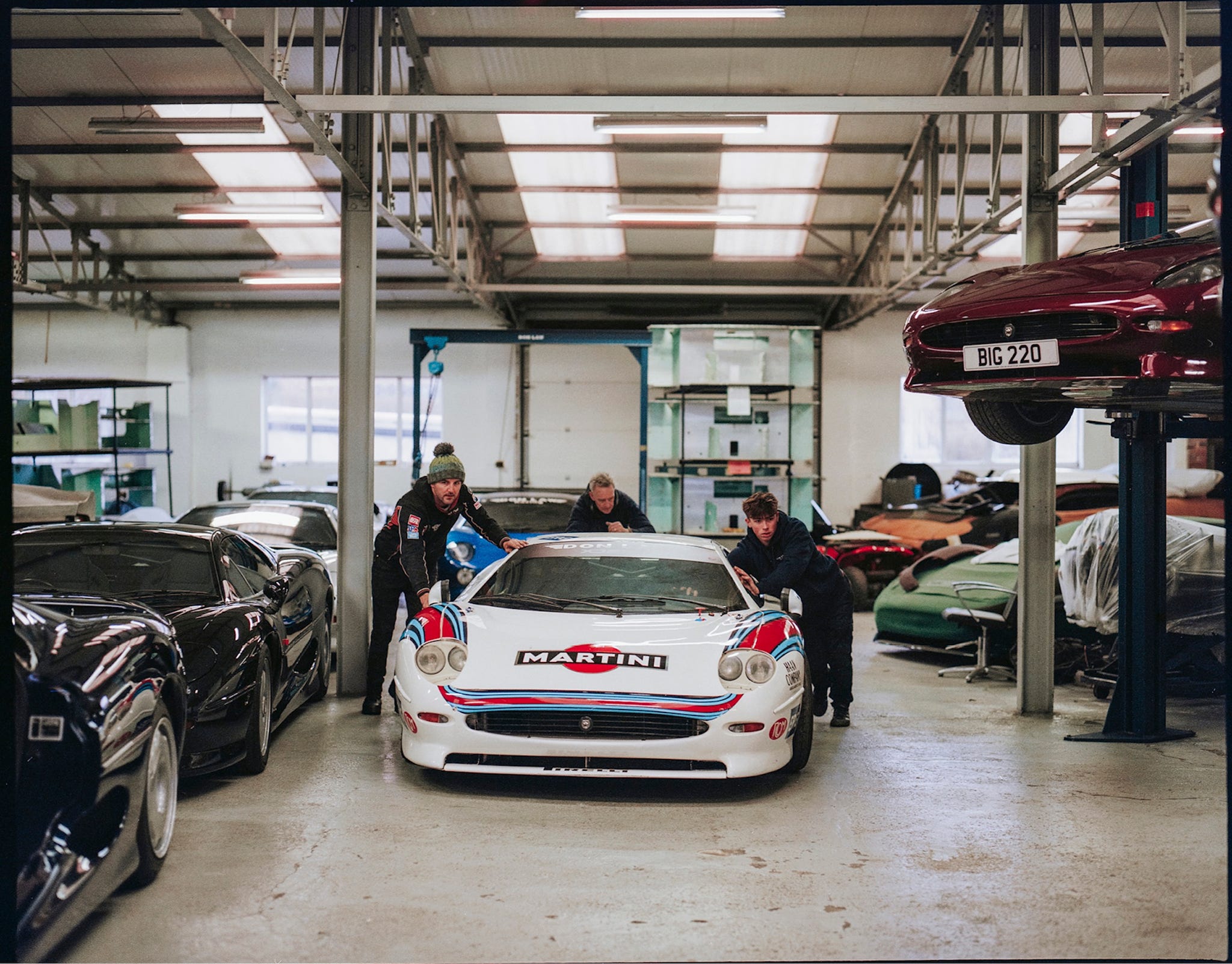 Mechanics performing maintenance on a Jaguar XJ220 inside a professional garage.