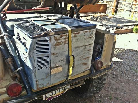 A 12V refrigerator sitting on the ground next to a camper at a remote campsite.