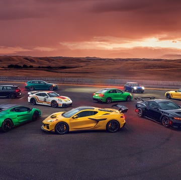 A group of high-performance sports cars gathered on a racetrack at sunset.