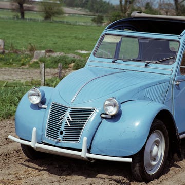 A vintage grey 1959 Citroën 2CV parked in a sunlit outdoor setting.