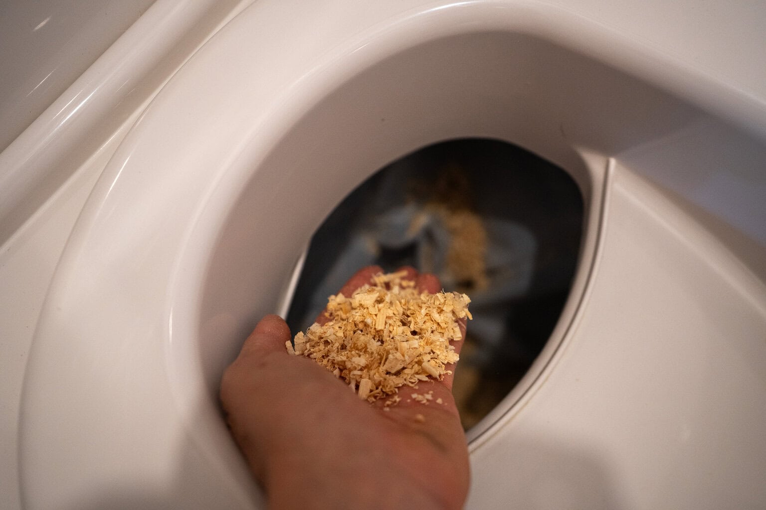 A hand adding wood chips into the solids bin of the composting toilet.