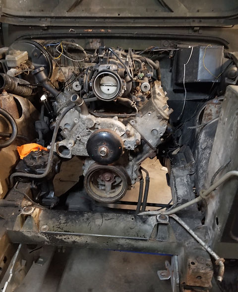 A GM LS3 V8 engine being lowered into a stripped Land Rover Defender chassis.