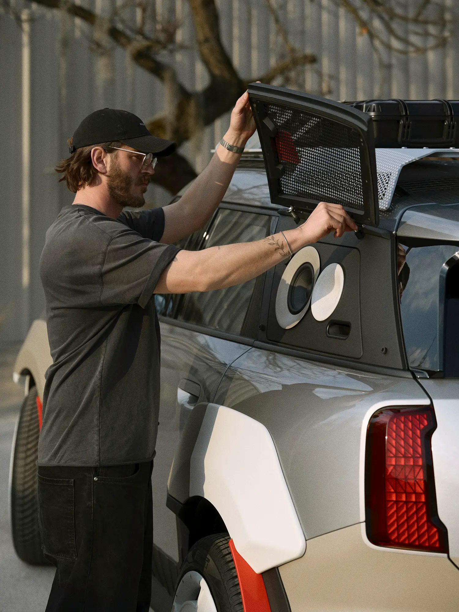 A hand adjusting the hinged mesh cover of the integrated outdoor speaker system.