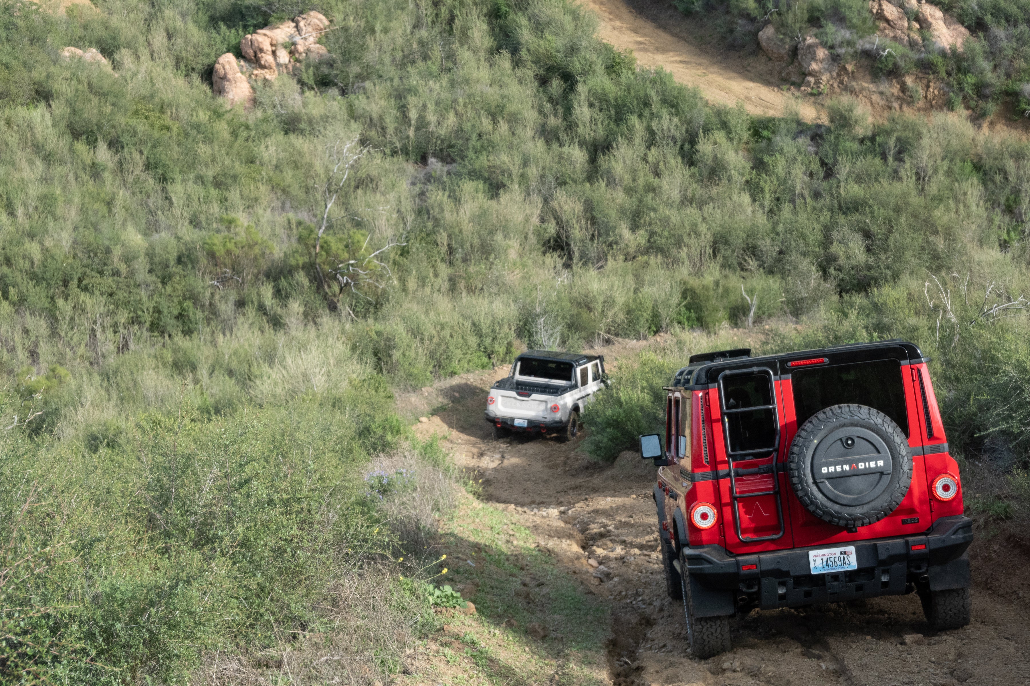Ineos Grenadier driving through a tight curve on a dusty off-road trail.